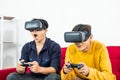 Two young teenager Asian men feeling excite, sit on the sofa couch while playing joy stick console game and wearing virtual