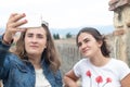 Two young teenagers taking a selfie photograph with the monument of the aqueduct of Segovia in Spain as background