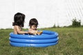 Two young toddler female sisters playing on a blue small paddling pool in the grass Royalty Free Stock Photo
