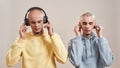 Two young twin brothers in casual wear with tattoos and piercings listening music in headphones and wireless earphones Royalty Free Stock Photo