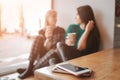 Two young woman chatting in a coffee shop. Two friends enjoying coffee together. Their smartphones lying in pile on Royalty Free Stock Photo