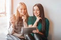 Two young woman chatting in a coffee shop. Two friends enjoying coffee together. One girl uses a tablet. Royalty Free Stock Photo