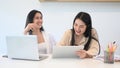 Two young woman designer in casual wear laughing while working with laptop at modern office. Royalty Free Stock Photo