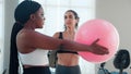 Two young woman in sportswear workout routines using exercise ball in fitness gym with trainer, instructor explaining and training Royalty Free Stock Photo