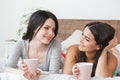 Lesbian couple in bedroom at home lying drinking tea talking playful