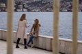 Two young women chatting near sea side. Outside behind the fence.