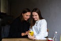 Two young women communicate and look into smartphone in cafe on terrace