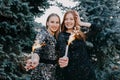Two young women in evening dress holding sparklers in hand on fir tree background outdoor. Closeup of two beautiful girl holding