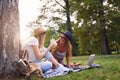 Two female friends sitting on the grass, talking and using laptop Royalty Free Stock Photo