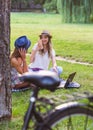 Two female friends sitting on the grass, talking and using laptop Royalty Free Stock Photo