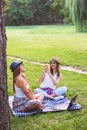 Two female friends sitting on the grass, talking and using laptop Royalty Free Stock Photo