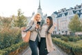 Two young women having fun, looking at the smartphone laughing, sunny autumn day, city background, golden hour