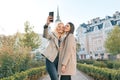 Two young women having fun, looking at the smartphone laughing, sunny autumn day, city background, golden hour