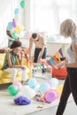 two young women holding string with party garlands and their male friends decorating room