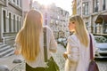 Two young women with laptop bags walking along street of sunset city, back view