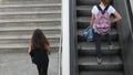 Two young women with rucksacks going up using stairs and escalator