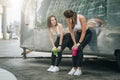 Two young women runners stand leaning against trailer, rest after training, drink water, communicate. Girls have break.