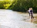 Two young women salmon fishing in small river in Alaska.