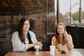 Two young women sit in an open cafe in the city