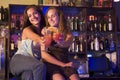 Two young women sitting on a bar counter, toasting Royalty Free Stock Photo