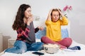 Two young women are sitting on the bed, eating popcorn and talking about something. The concept of quarantine, work from home,