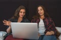 Two young women sitting in bed, looks at laptop screen and talking. Female couple or just friends spend time together Royalty Free Stock Photo