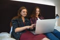 Two young women sitting in bed, looks at laptop screen and talking. Female couple or just friends spend time together Royalty Free Stock Photo