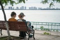 Two young women sitting on bench under big tree by the lake in city Royalty Free Stock Photo