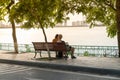 Two young women sitting on bench under big tree by the lake in city Royalty Free Stock Photo