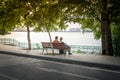 Two young women sitting on bench under big tree by the lake in city Royalty Free Stock Photo
