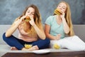 Two young women sitting at coach eating fast food Royalty Free Stock Photo
