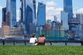 Two young women sitting in the grass in Pier A Park in Hoboken, NJ. Behind them and across the Hudson River are the skyscrapers of Royalty Free Stock Photo