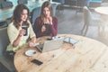 Two young women are sitting at round wooden table in cafe,drinking coffee and looking at laptop screen. Royalty Free Stock Photo