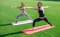 Two young women in sportswear doing yoga on the grass at the stadium