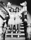 Two young women stepping down a staircase waving their western hats