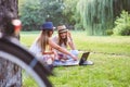 Two young women students in park sitting on grass talking, using laptop Royalty Free Stock Photo