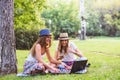 Two young women students in park sitting on grass talking, using laptop Royalty Free Stock Photo