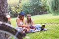 Two young women students in park sitting on grass talking, using laptop Royalty Free Stock Photo