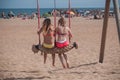 Two young women in swimsuit on a swing on the beach