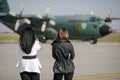 Two young women watch a military cargo plane on the runway of an airport. Royalty Free Stock Photo