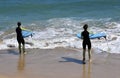 Two young women wearing wetsuits entering the sea carrying surf boards