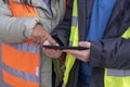 Two young workers in orange and yellow vests  lookig at tablet computer and discusses a project Royalty Free Stock Photo