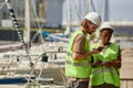 Two young workers wearing hardhats standing in yacht docks