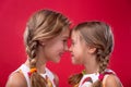 Twoloving sisters look at each other head-on and smiling on isolated red background. Close-up portrait of happy girls Royalty Free Stock Photo