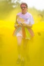 Adult female runner runs through thrown yellow paint on a charity colour paint run.