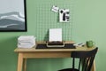 Typewriter, stack of papers and mood board on wooden table near pale green wall. Writer`s workplace