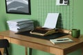 Typewriter, stack of papers and mood board on wooden table near pale green wall. Writer`s workplace