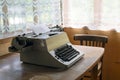 A typewriter stands on a table, next to a vintage chair. Retro interior with wooden walls, tulle curtains on the windows