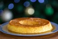 Typic caramelized condensed milk pudding with eggs, in selective focus on a blurred background of decorated Christmas tree. Royalty Free Stock Photo