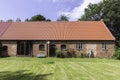 A typical barn with red brick walls and modern red roof surrounded with gr